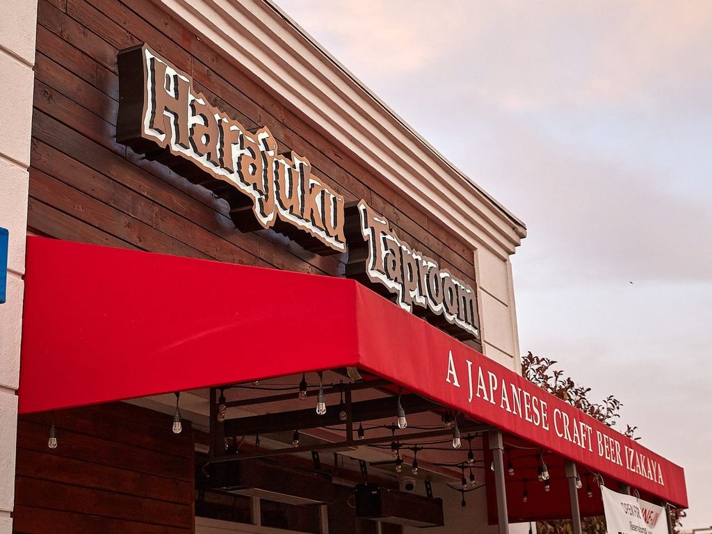 Exterior view of Harajuku Taproom, a Japanese craft beer izakaya, featuring a red awning and wooden facade. The restaurant's name is prominently displayed on the building.