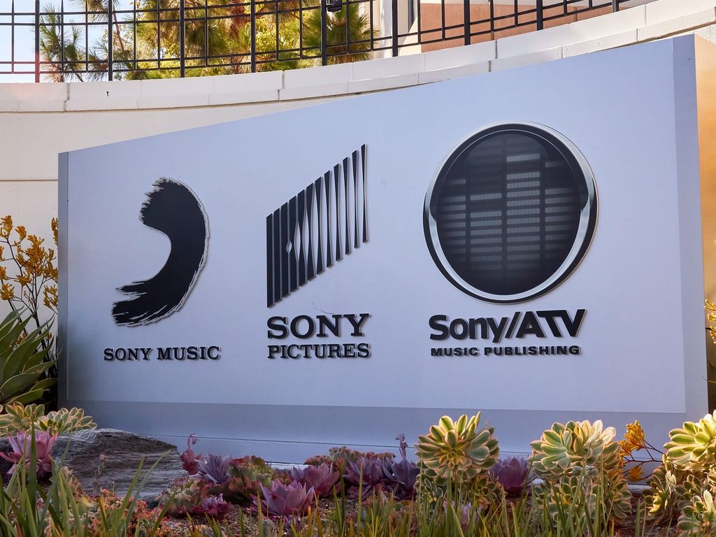 A sign displays the logos for Sony Music, Sony Pictures, and Sony/ATV Music Publishing, surrounded by various plants and flowers.