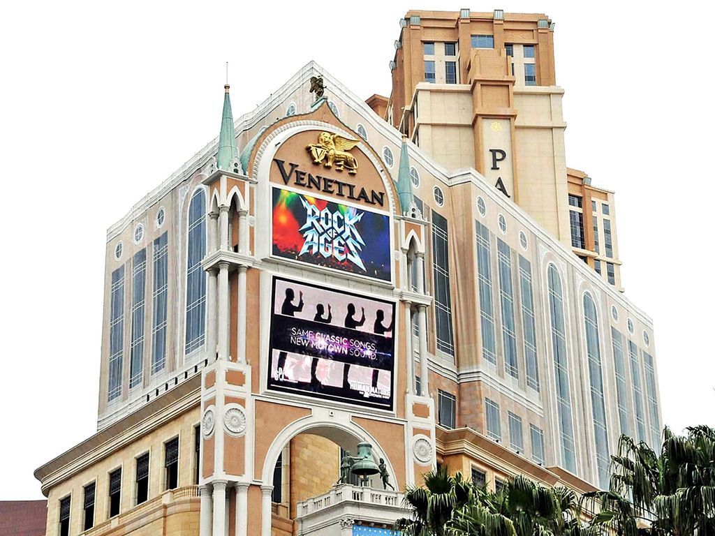 The Venetian Macao hotel and casino building is shown, featuring its distinctive architecture and large digital displays on the facade.